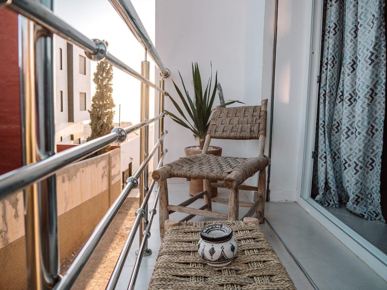 A woven chair and small ceramic pot on a balcony in warm evening light